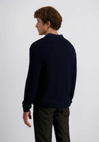 Navyfarbener Strickpullover mit Kragen, gerippten Bündchen und glatter Textur. Über dunklen Hosen getragen, von hinten betrachtet.