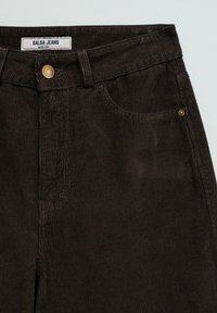 Pantalones vaqueros de pana marrón de pierna ancha con un botón de metal, textura acanalada prominente y bolsillos delanteros. La etiqueta dice "Salsa Jeans."