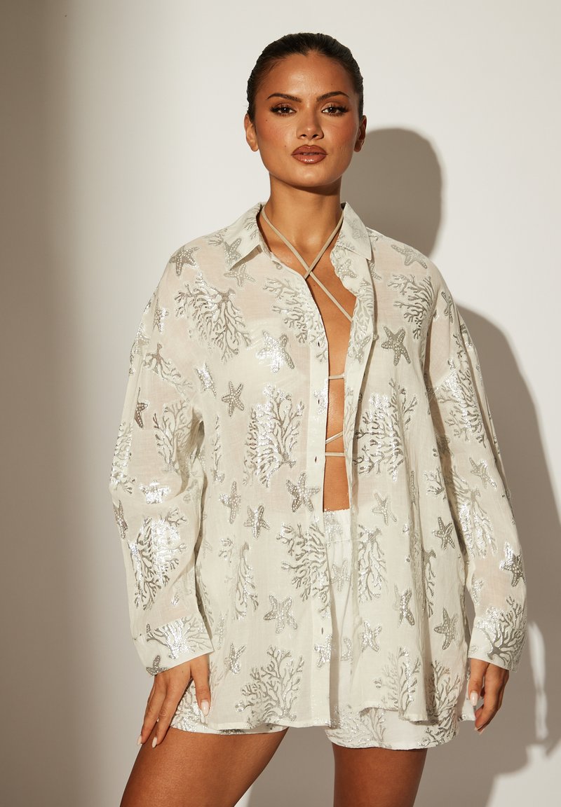 Camisa blanca y transparente de botones con bordado de coral plateado y estrellas de mar, de manga larga y corte holgado. Combínala con pantalones cortos a juego.