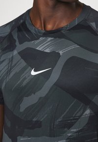 Camiseta atlética negra y verde oscuro con un patrón de camuflaje, cuello redondo y un logo blanco de Nike en el pecho.