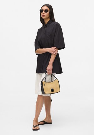 Svart kortärmad knappskjorta, krämfärgad kjol, svarta flip-flops och en tvåfärgad handväska med vävd textur och logodetalj.