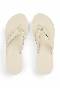 Chanclas beige con suela texturizada, tiras de tela con un borde festoneado y un detalle de logo en la tira.