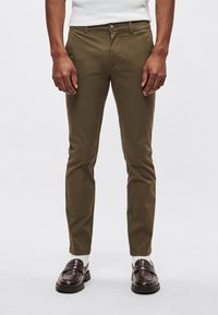 Khaki chino's met een slim fit, voorzien van een knoopsluiting, voorzakken en een zachte katoenmix. Gecombineerd met donkerbruine loafers en lichte sokken.