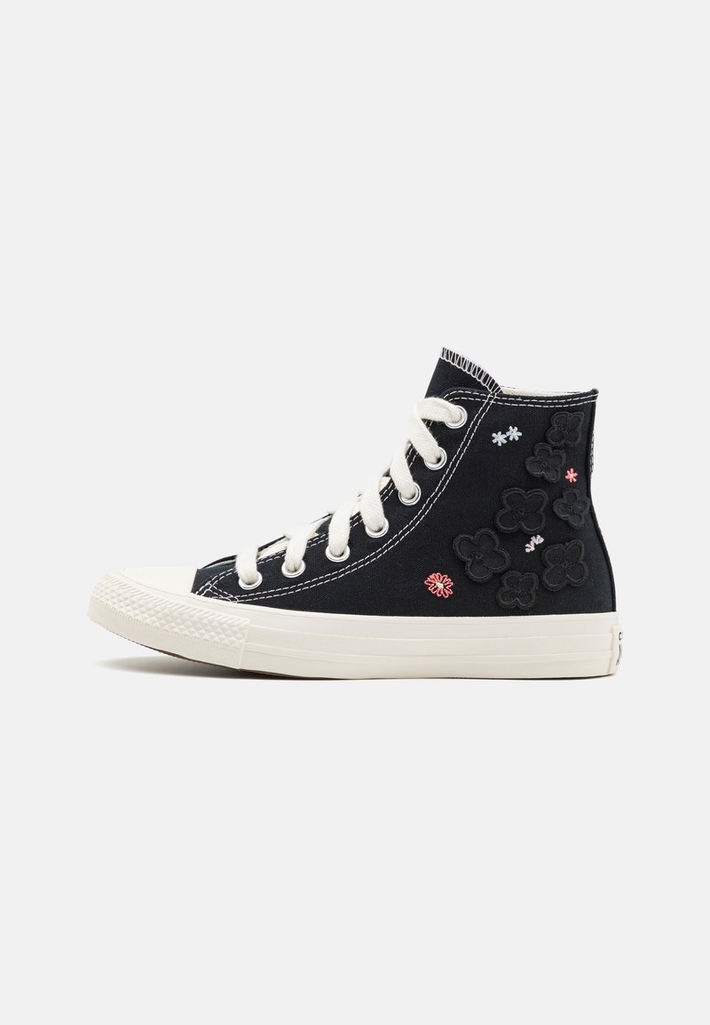 Basket montante en toile noire avec lacets blancs, semelle blanche épaisse et petits motifs floraux brodés sur le côté.