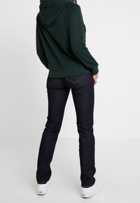 Mörkblå denimjeans med rak passform, tillsammans med en mörkgrön hoodie och vita sneakers. Hoodien har en känguruficka och snörning.