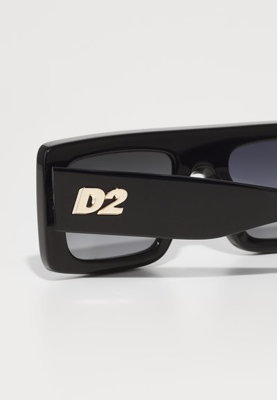 Black rectangular sunglasses with gradient dark lenses. Features a gold “D2” logo on the arm. Smooth, glossy plastic material.