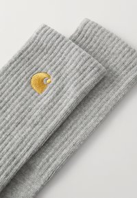 Sive rebraste čarape s mekim teksturama. Sadrže zlatni vezeni logo s jedne strane. Dizajn je jednostavan, funkcionalan i uniseks.