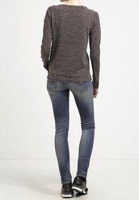 Mörkgrå stickad tröja med långa ärmar, kombinerad med ljusblå skinny jeans och svarta sneakers. Slät textur, figurnära design.