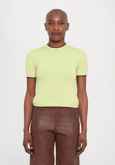 Top à manches courtes en tricot côtelé de couleur vert clair avec des bordures contrastantes en marron. Associé à un pantalon en cuir brun. Col rond simple.