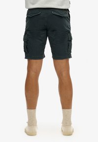 Mørkegrønne cargoshorts med påsyede lommer, lige snit og opkrøllede kanter, lavet af bomuldsstof. Har en struktureret overflade og knælangt design.