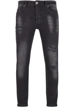 Jeans en denim noir à coupe slim, présentant des détails déchirés et des patches effilochés, un léger délavage, et une fermeture standard par bouton et zip.