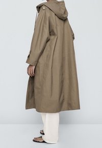 Long, hooded coat in light brown fabric. Features side pockets, button accents on shoulders, and a loose, relaxed fit.