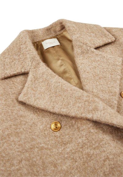 Beżowy płaszcz z mieszanki wełny o teksturowanym wykończeniu, z zapięciem na złote guziki i satynową podszewką. Zasuwany kołnierz.