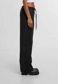 Zwarte joggingbroek met een ontspannen pasvorm, gemaakt van gladde stof en voorzien van zijzakken, gecombineerd met chunky zwarte schoenen.