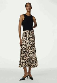 Beige en bruine midi-jurk met luipaardprint, gemaakt van een gladde stof, gecombineerd met een nauwsluitend zwart tanktop en zwarte hakken.