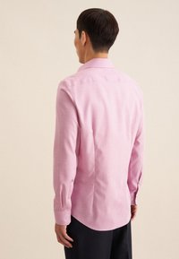 Camicia button-up rosa chiaro con yoke posteriore, maniche lunghe e polsini regolabili. La texture liscia e il taglio su misura creano una silhouette pulita.
