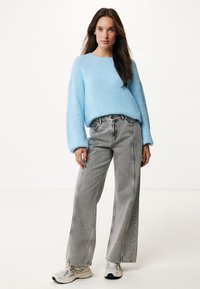 Lichtblauwe gebreide trui met lange, aansluitende mouwen, gecombineerd met hooggewaist grijze wijde jeans en beige sportschoenen.