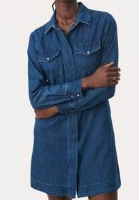 Tumman sininen farkkukangaspaita-mekko, jossa on napitus edessä, kaksi rintataskua, pitkät hihat ja rento istuvuus suoran helman kanssa.