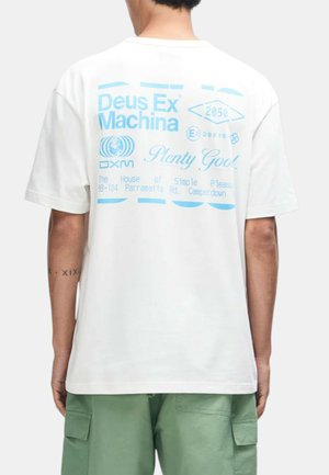 Persona que lleva una camiseta blanca con texto azul "Deus Ex Machina" y gráficos en la espalda, combinada con pantalones cortos cargo verdes.