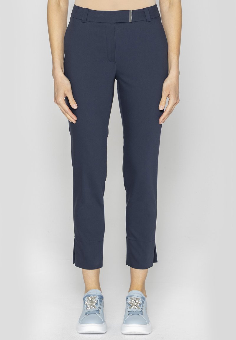 Granatowe spodnie stretch o slim fit, z zamkiem błyskawicznym z przodu i małymi rozporkami po bokach na dole. W zestawie z jasnoniebieskimi trampkami.