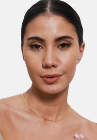 Gold-toned necklace with a smooth, thin, curved design resting on the collarbone, against a bare skin background.