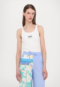Hvit ribbestrikket tank top med en svart "Moschino Jeans" logo-patch, kombinert med mønstrede blå og hvite vide bukser med snøring i livet.