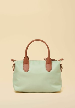 Maiza zaļā soma ar brūniem ādas rokturiem un akcentiem, attēlota pret bēša fona.