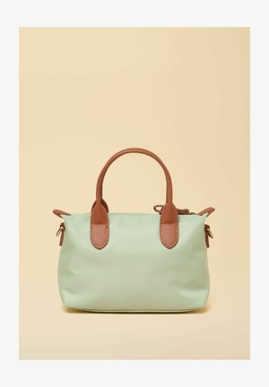 Maiza zaļā soma ar brūniem ādas rokturiem un akcentiem, attēlota pret bēša fona.