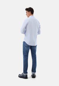 Hellblaues Langarmhemd mit Kragen, kombiniert mit dunkelblauen Jeans und schwarzen Schuhen. Das Hemd hat einen geraden Saum und geknöpfte Manschetten.
