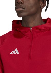 Felpa sportiva rossa con cappuccio, caratterizzata da un collo con zip, una trama morbida e dettagli del logo bianco. Include un cappuccio e cuciture rinforzate sulle spalle.
