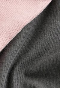 Deux échantillons de tissu : un tricot côtelé rose doux et un tricot lisse gris foncé, chacun affichant une texture visible et des coutures régulières.