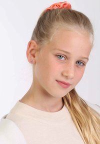 Sprankelende roze stud earrings, een lichtbeige trui en een perzikkleurige scrunchie in blond haar. Gladde textuur, heldere kleurcontrast.