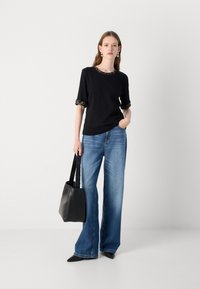 Top noir avec un bord décoré au niveau du col et des manches, associé à un jean large bleu clair et un sac en cuir noir.