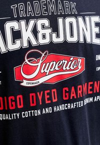 Κείμενο σε σκούρο ύφασμα αναγράφει «Trademark Jack & Jones Superior Copenhagen Indigo Dyed Garment Quality Cotton and Handcrafted Denim.»