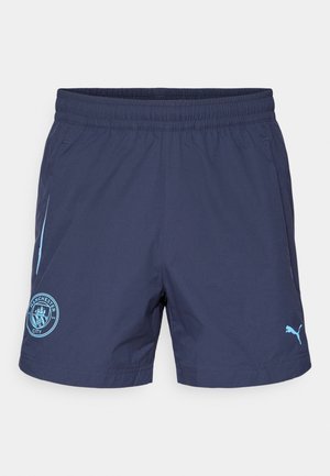 Shorts bleumarin cu talie elastică, logo Puma de culoare albastru deschis și un emblemă Manchester City de culoare albastru deschis pe piciorul stâng.