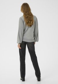 Pull gris avec des manches bouffantes texturées, associé à un pantalon noir droit et des bottes à talons blocs, vu de dos.