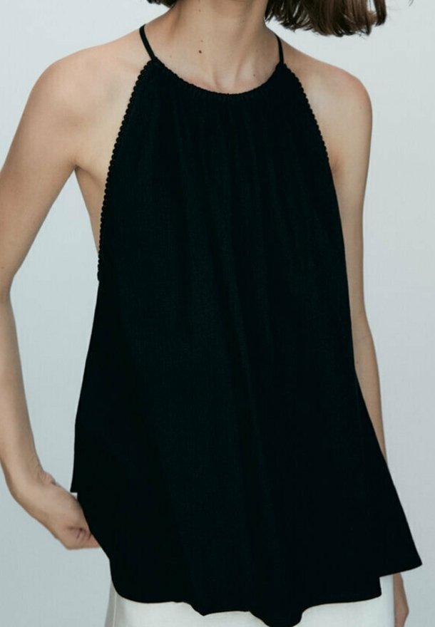 Haut halter noir en tissu texturé, avec de fines bretelles et un décolleté froncé, créant une silhouette ample et fluide.