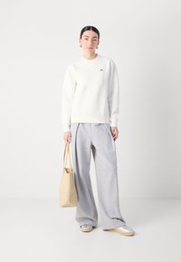 Felpa bianca con polsini e fondo a coste, abbinata a pantaloni della tuta grigi larghi. Una borsa a spalla beige e scarpe argentate completano l'outfit.