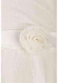 Robe blanche en tissu texturé avec des motifs floraux, accentuée par une ceinture en satin ornée d'une rose en tissu de couleur assortie.