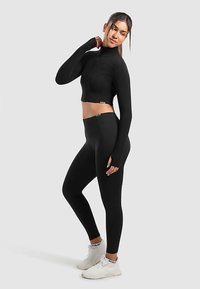 Black long-sleeve crop top with zip closure and fitted black leggings. Both pieces made of smooth, stretchy material. White sneakers complete the outfit.