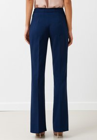 Pantalones de traje azul marino con una tela suave, pierna acampanada y una cinturilla ligeramente texturizada, con dos bolsillos traseros y un acabado limpio.