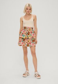 Débardeur crème côtelé avec des boutons à l'avant associé à une jupe en couches à motifs floraux roses, ornée de fleurs vertes, jaunes et orange.
