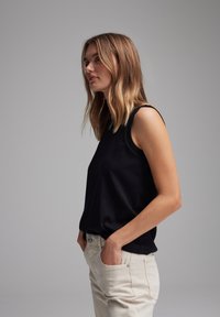 Top senza maniche nero in un tessuto liscio, con scollatura rotonda e vestibilità comoda, abbinato a pantaloni beige chiari per un contrasto.