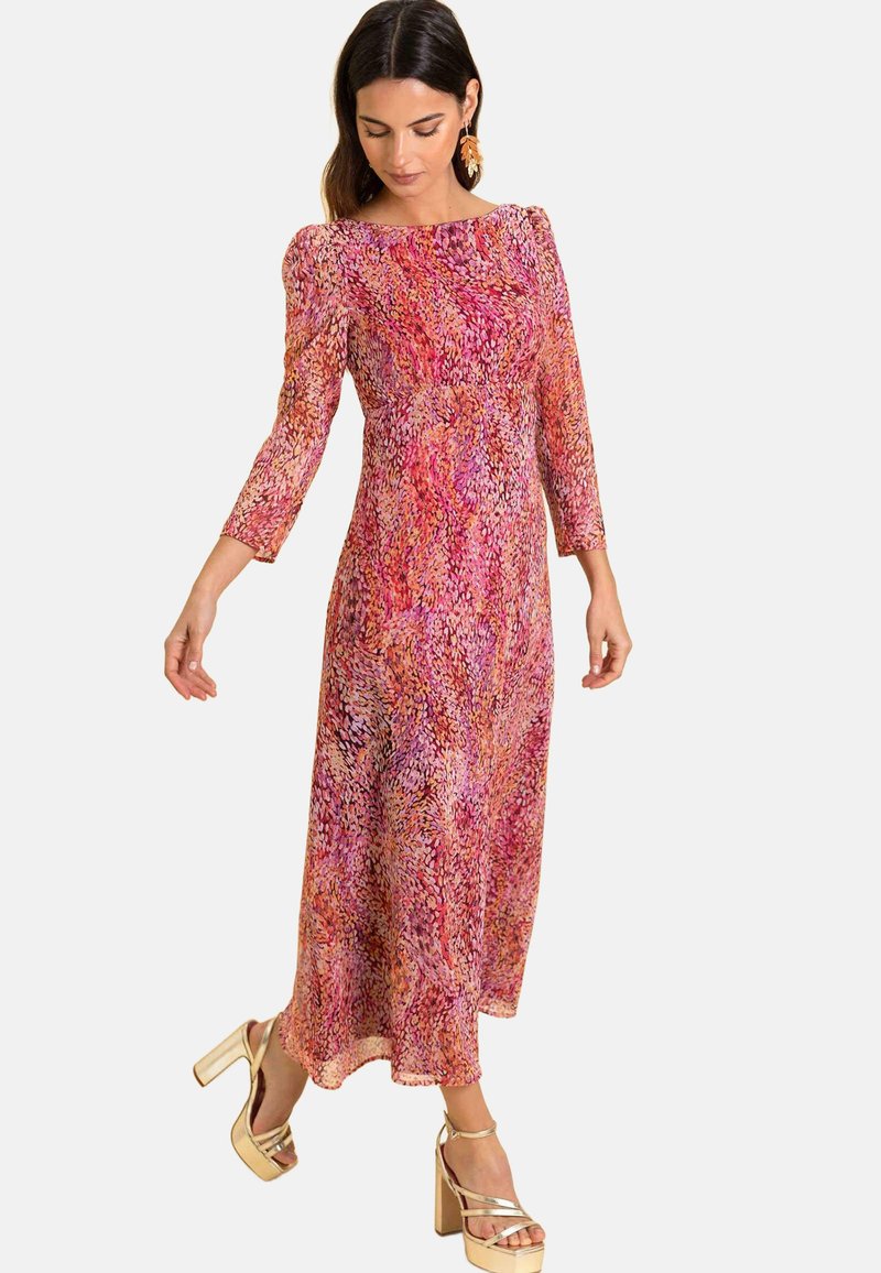 Maxikleid mit buntem Blumenmuster in Pink- und Orangetönen, mit Dreiviertelärmeln und fließender Silhouette. Goldene Plateausandaletten.