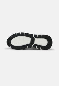 Semelle de chaussure de sport noire avec des accents en caoutchouc blanc, présentant un motif texturé et des rainures pour la traction. Taille indiquée : 42.