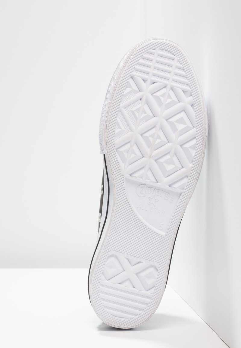 Baskets noires en toile avec une semelle en caoutchouc blanc texturé présentant un logo en étoile et un motif de semelle géométrique, mises en valeur par des œillets argentés.