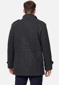 Mørk grå ullblandingsfrakk med høy krage, knappede mansjetter og skreddersydd bakparti med sømdetaljer. Klassisk, strukturert design.