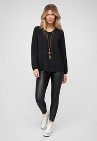 Black long-sleeve top with a round neckline, paired with black shiny leggings and white sneakers. Features a pendant necklace with accents.