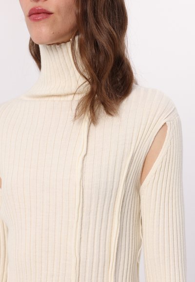 Kared, pika-sleeve ülikond off-white värviga, millel on kõrge kaelus ja asümmeetrilised lõiked õlgadel, esitades tekstureeritud kanga.