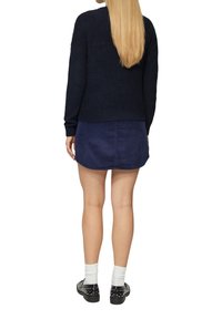 Marineblauwe gebreide trui, met een geribbelde hals; gecombineerd met een marineblauwe corduroy rok; zwarte schoenen met zilveren studs; witte crew-sokken.